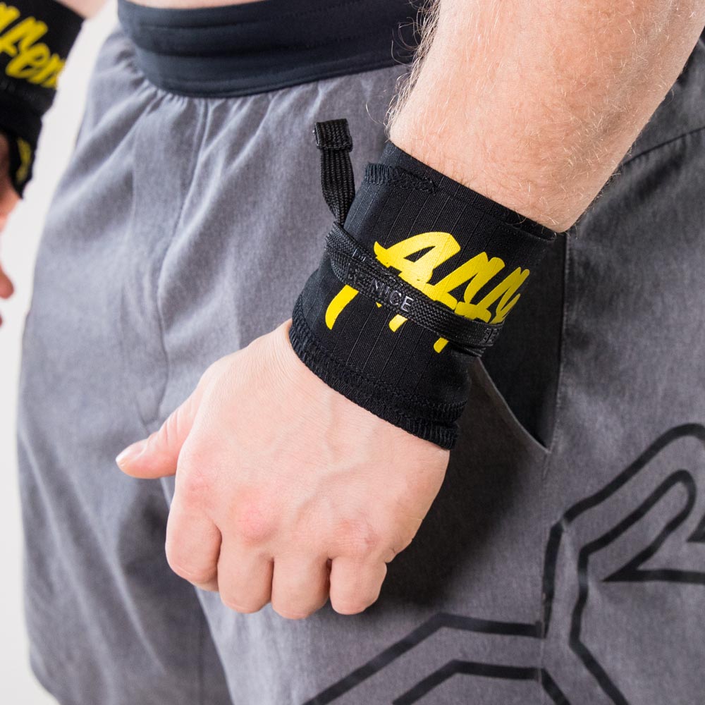 affenhand-handgelenksbandagen-flexibel Nahaufnahme einer Person, die Affenhand Handgelenkbandagen in Schwarz-Gelb trägt, mit dem gelben Schriftzug „Affenhand“ auf schwarzem Stoff.