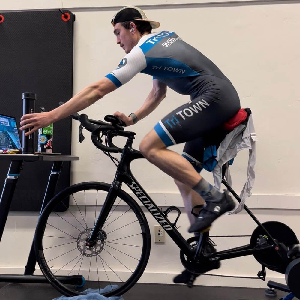 Triathlet greift während Indoor-Cycling zur schwarzen AVA Cooling Bar auf dem Tisch – gezielte Kühlung beim Ausdauertraining