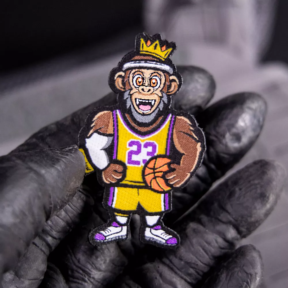 Hand hält einen Klett-Patch, auf dem ein springender Gorilla mit einem Basketball abgebildet ist.